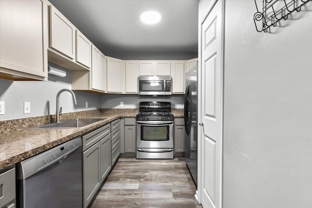 kitchen with wood finished floors, dark countertops, a sink, appliances with stainless steel finishes, and gray cabinetry