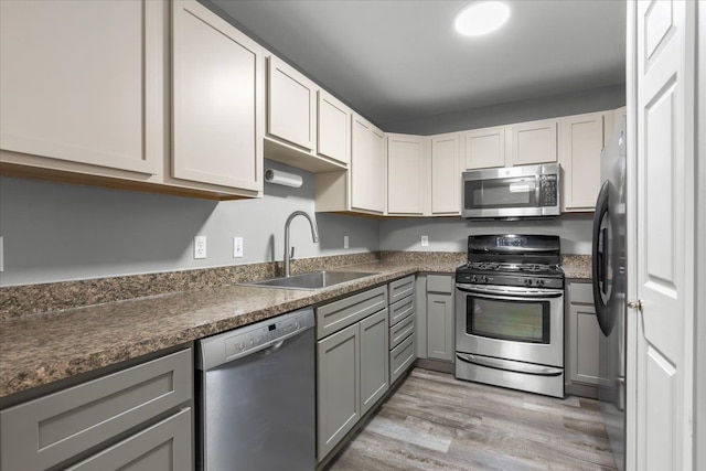 kitchen with a sink, light wood-style flooring, gray cabinetry, and stainless steel appliances