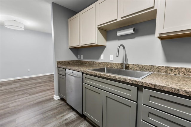 kitchen featuring wood finished floors, dark countertops, a sink, and dishwasher