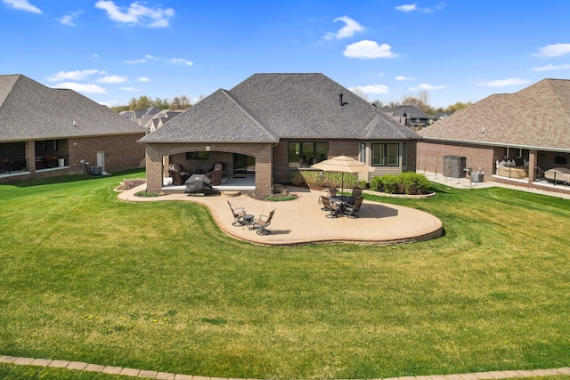rear view of house featuring a lawn, a patio, a shingled roof, and brick siding