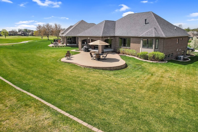 back of property with a patio, a lawn, roof with shingles, and brick siding