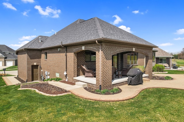 rear view of house with a yard, brick siding, a patio area, and roof with shingles