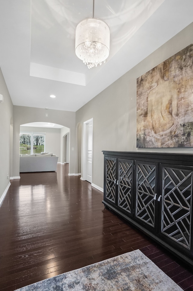 interior space with hardwood / wood-style floors, baseboards, recessed lighting, a raised ceiling, and arched walkways