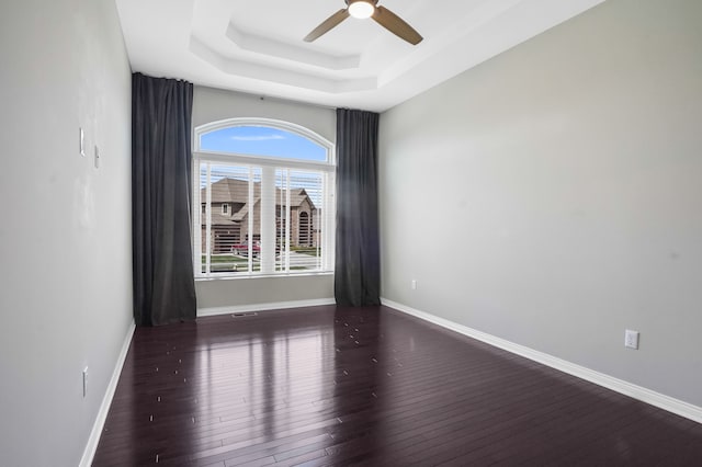 spare room featuring a raised ceiling, baseboards, a ceiling fan, and wood finished floors