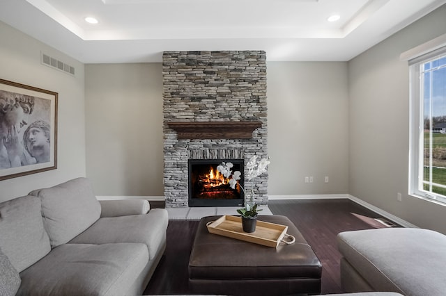 living area with dark wood-style flooring, a tray ceiling, visible vents, and a healthy amount of sunlight