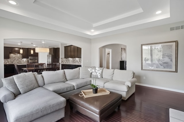 living area with visible vents, baseboards, recessed lighting, a raised ceiling, and arched walkways
