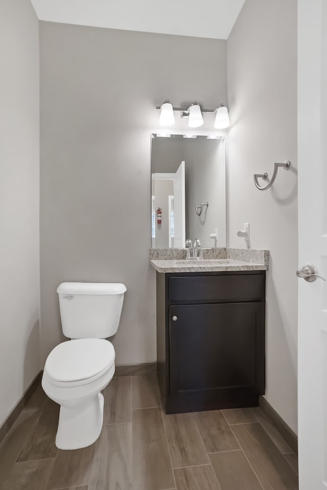 half bath featuring toilet, wood finish floors, baseboards, and vanity