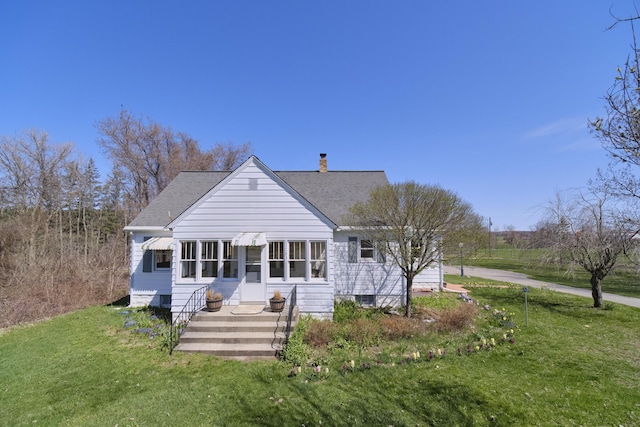rear view of property featuring roof with shingles, a chimney, and a yard