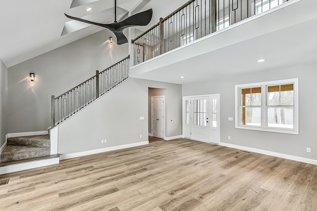 unfurnished living room with baseboards, a ceiling fan, a towering ceiling, and wood finished floors
