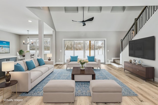 living area with vaulted ceiling, baseboards, light wood finished floors, an inviting chandelier, and stairs
