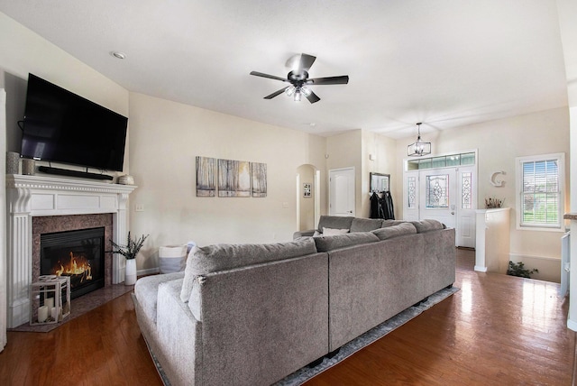 living room featuring arched walkways, ceiling fan, a fireplace with flush hearth, and dark wood-style floors
