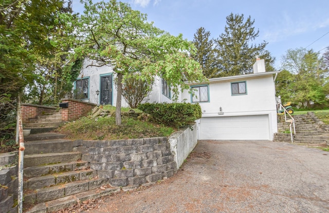 view of front of property with driveway, a chimney, an attached garage, stairs, and stucco siding
