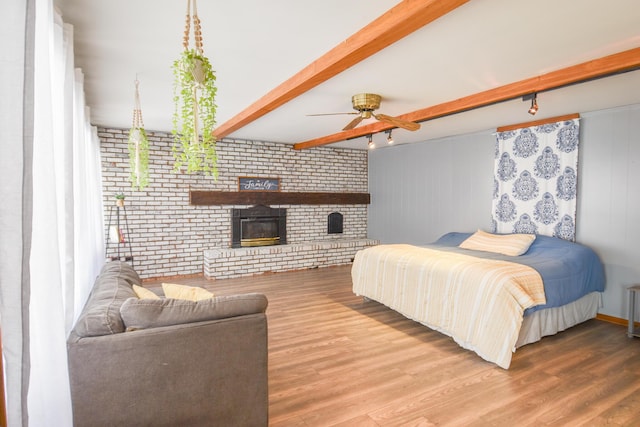 bedroom with a brick fireplace, beamed ceiling, and wood finished floors
