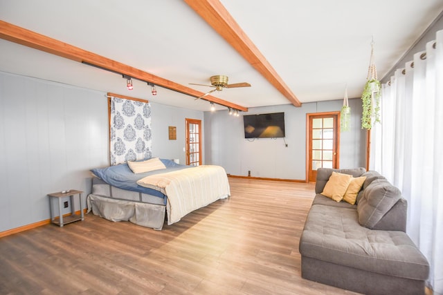 bedroom with baseboards, beam ceiling, multiple windows, and wood finished floors