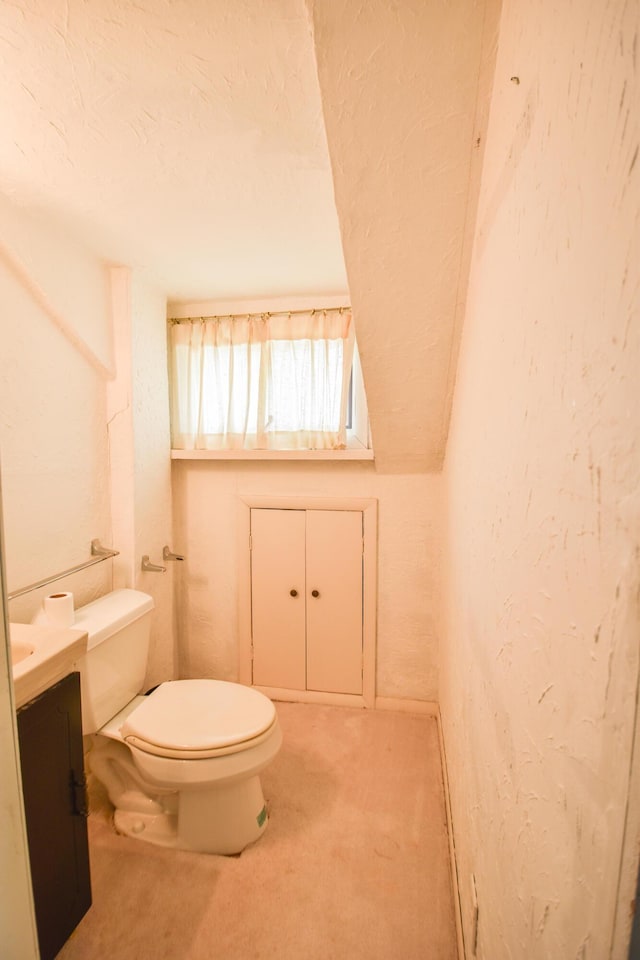 half bath with toilet, a textured ceiling, a textured wall, and vanity