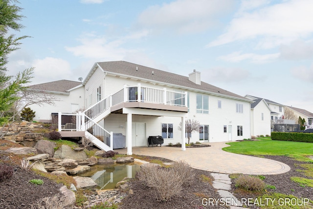 back of property featuring a wooden deck, a chimney, a patio area, a lawn, and stairway