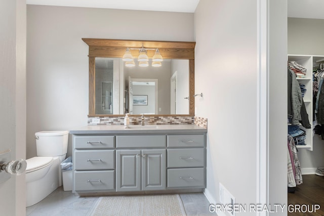 bathroom with a walk in closet, decorative backsplash, vanity, toilet, and a notable chandelier
