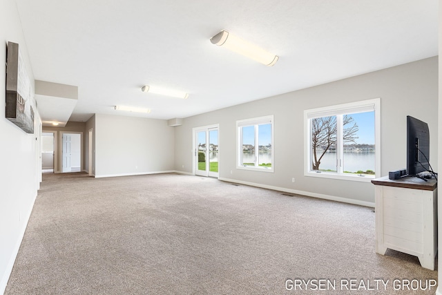 unfurnished living room with carpet flooring, baseboards, and a wealth of natural light