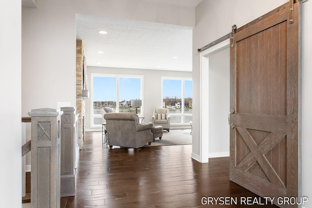 corridor with dark wood-type flooring, a barn door, baseboards, and recessed lighting