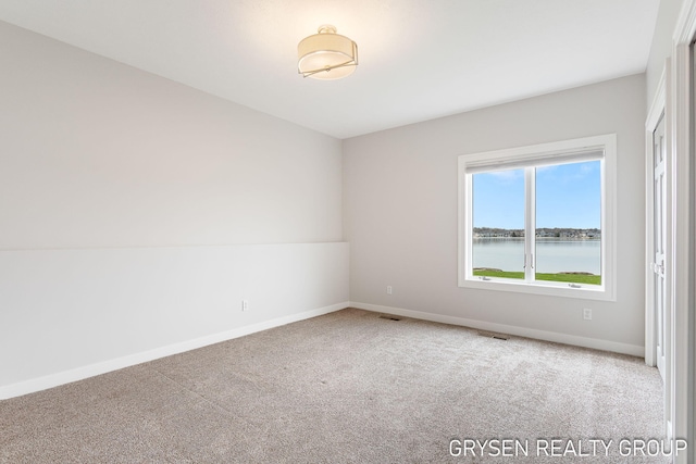 unfurnished room featuring carpet floors, a water view, baseboards, and visible vents