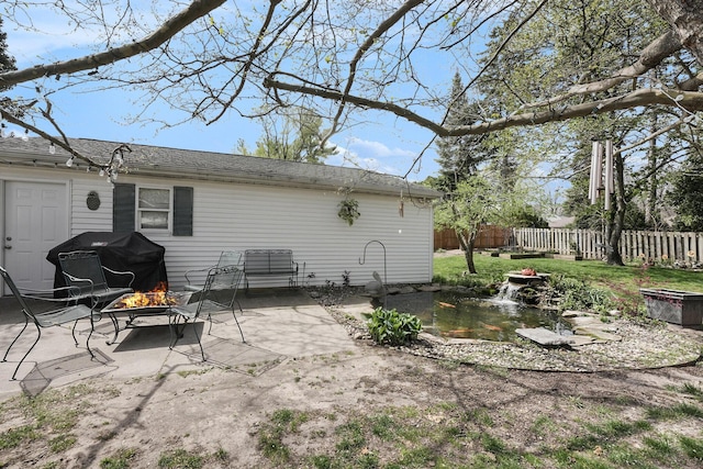 rear view of property featuring a garden pond, fence, a patio area, and an outdoor fire pit