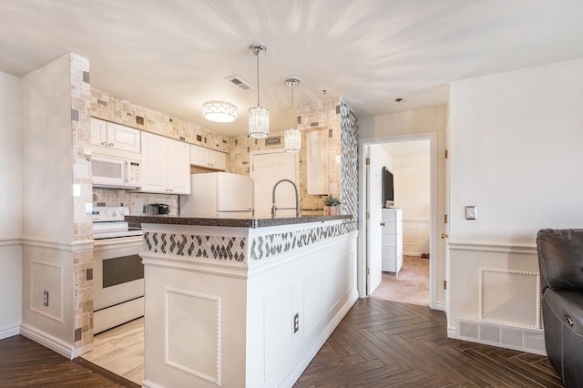kitchen with visible vents, a peninsula, dark countertops, white appliances, and a sink