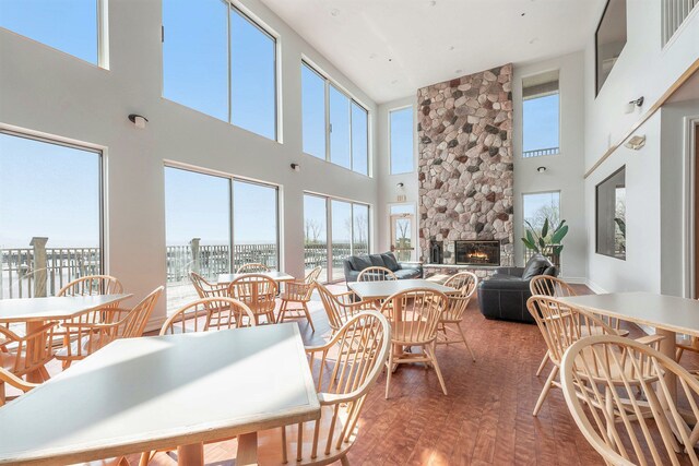 dining space with wood finished floors, visible vents, a stone fireplace, and a towering ceiling