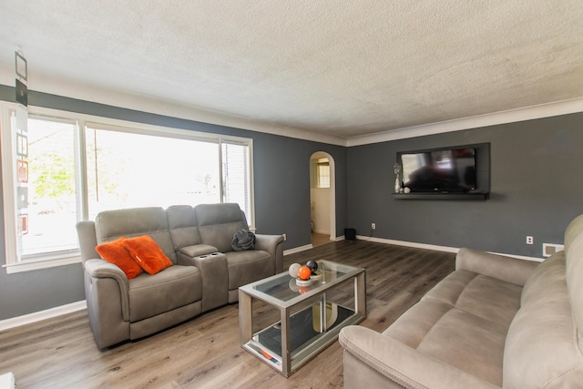 living room featuring arched walkways, a textured ceiling, wood finished floors, and a healthy amount of sunlight