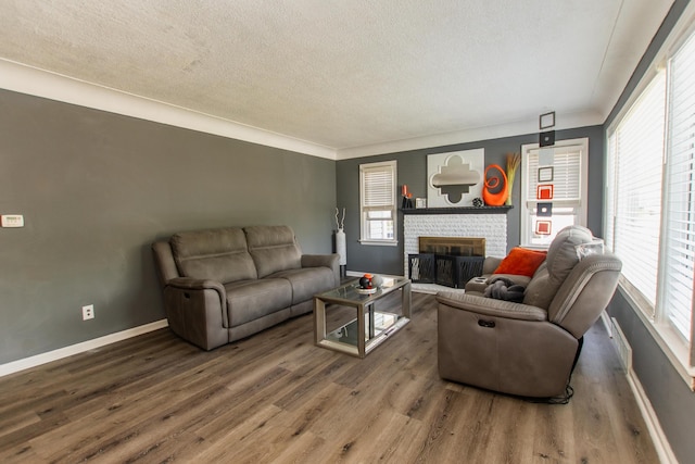 living area featuring a brick fireplace, a textured ceiling, plenty of natural light, baseboards, and wood finished floors