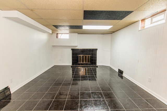 unfurnished living room featuring dark tile patterned floors, visible vents, a tiled fireplace, and a paneled ceiling