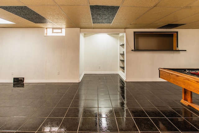 basement featuring billiards, built in features, dark tile patterned flooring, baseboards, and a drop ceiling