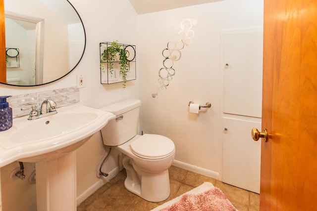 bathroom featuring a sink, tile patterned flooring, toilet, baseboards, and tasteful backsplash