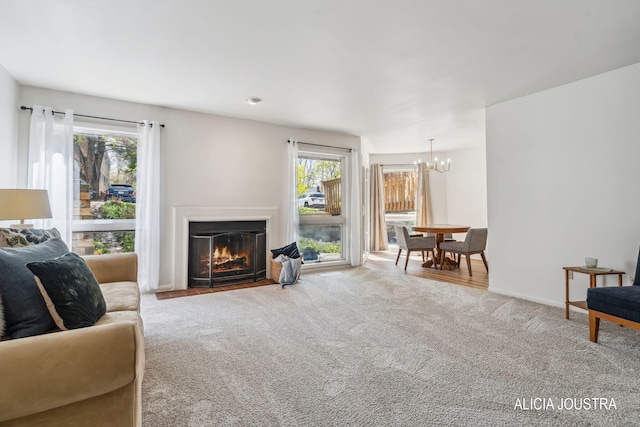 carpeted living room featuring baseboards, a fireplace with flush hearth, and a notable chandelier