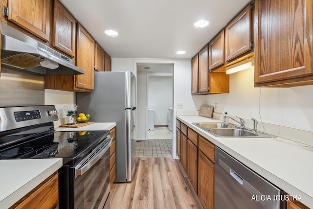kitchen with light wood-type flooring, light countertops, under cabinet range hood, a sink, and stainless steel appliances
