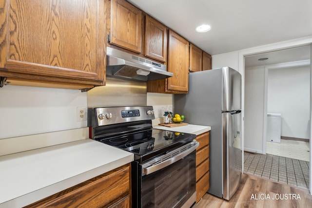 kitchen featuring brown cabinets, light countertops, under cabinet range hood, light wood-style floors, and stainless steel appliances