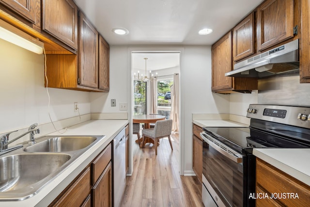 kitchen with brown cabinetry, appliances with stainless steel finishes, a sink, a notable chandelier, and under cabinet range hood