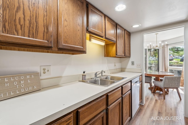 kitchen with stainless steel dishwasher, brown cabinetry, a sink, light wood-style flooring, and a notable chandelier