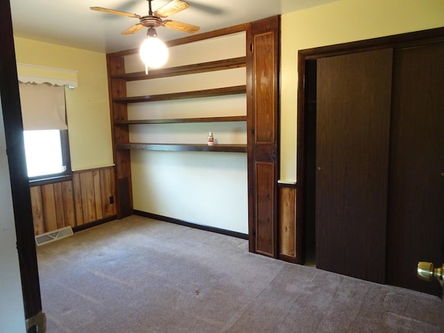 spare room with a ceiling fan, visible vents, wood walls, baseboards, and carpet flooring