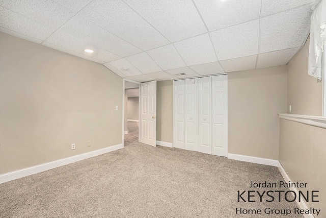 unfurnished bedroom with baseboards, carpet flooring, a drop ceiling, and a closet