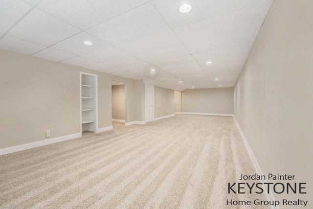 finished below grade area with baseboards, a drop ceiling, recessed lighting, built in shelves, and carpet