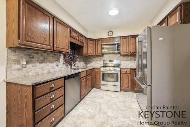 kitchen with brown cabinets, appliances with stainless steel finishes, a sink, and light stone counters