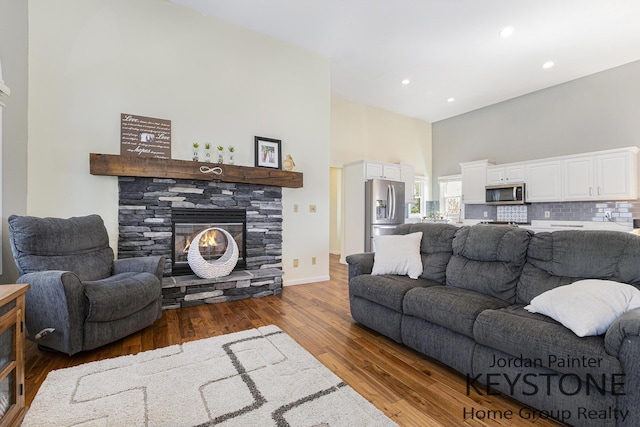 living room featuring a stone fireplace, a towering ceiling, wood finished floors, baseboards, and recessed lighting