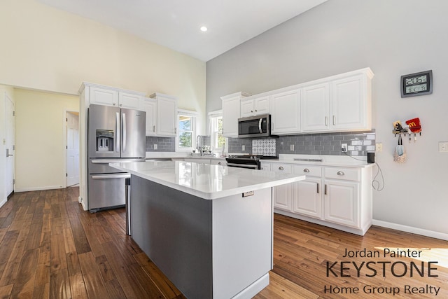 kitchen with appliances with stainless steel finishes, white cabinets, a center island, and backsplash