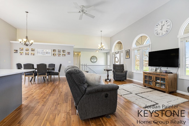 living room with baseboards, wood-type flooring, ceiling fan with notable chandelier, and a towering ceiling
