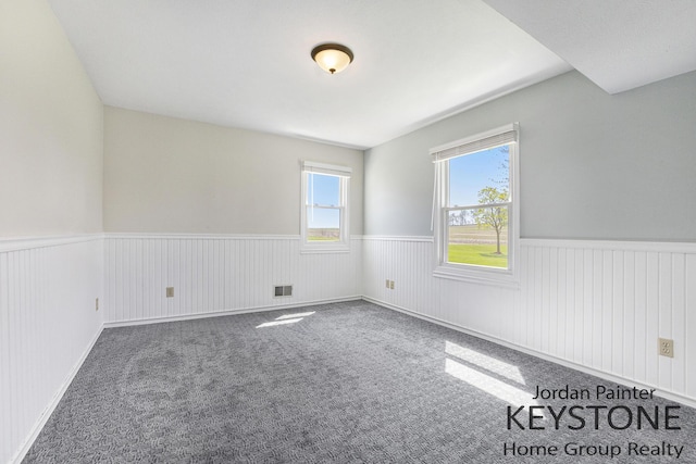 empty room with visible vents, carpet, and a wainscoted wall