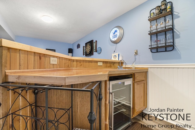 bar featuring beverage cooler, a wainscoted wall, and a bar