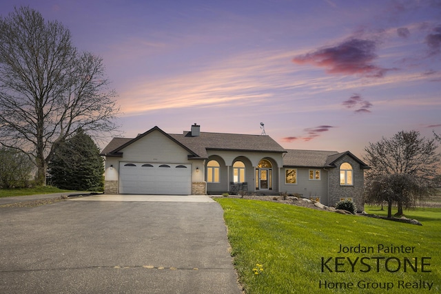 single story home featuring a shingled roof, an attached garage, a chimney, a yard, and driveway