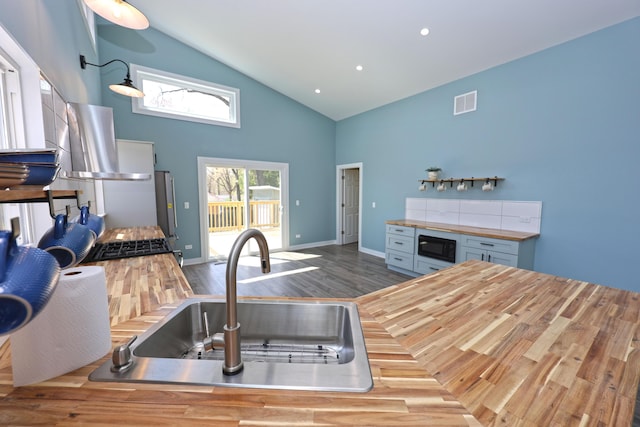 kitchen with visible vents, wood finished floors, butcher block countertops, high vaulted ceiling, and a sink