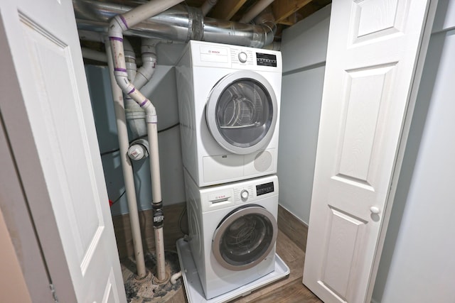 laundry area featuring stacked washer / drying machine, wood finished floors, and laundry area
