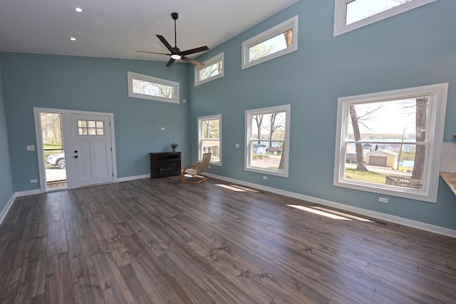 unfurnished living room featuring ceiling fan, baseboards, dark wood-style floors, a high ceiling, and recessed lighting